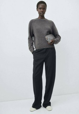 Gray knitted sweater with a round neckline, paired with black pinstripe trousers. The model holds a small gray clutch, wearing white slip-on shoes.