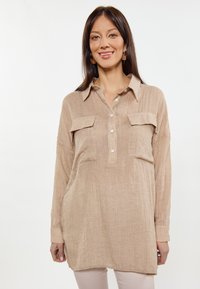 Camicia in lino beige con maniche lunghe, chiusura con bottoni e due tasche sul petto. Vestibilità rilassata con finitura testurizzata e dettagli di cucitura sottili.