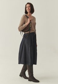 Pull marron clair ajusté avec un col en V, associé à une jupe trapèze en denim foncé avec des boutons sur le devant et un sac à bandoulière en cuir marron.