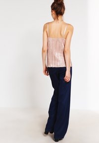 Jasnoróżowy top na cienkich ramiączkach z teksturowanymi pionowymi fałdami, zestawiony z luźnymi granatowymi spodniami typu wide-leg. Gładka tkanina, minimalistyczny design.