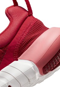 Gros plan d’un talon de chaussure de sport rouge avec col rembourré, tissu texturé et semelle blanche segmentée avec un soutien du talon rose.