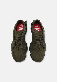 Sneakers in suede verde con una finitura strutturata, punta rotonda e suola in gomma. Presentano lacci e una linguetta sul tallone. Marchio del sottopiede rosso visibile.