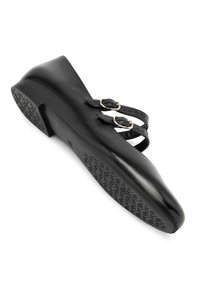 Schwarzer flacher Schuh mit runder Zehenpartie, strukturiertem Sohlenprofil und zwei verstellbaren Riemen mit silbernen Schnallen. Glattes Lederfinish, minimalistisches Design.