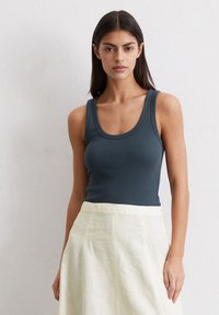 Débardeur côtelé bleu marine avec un décolleté arrondi, associé à une jupe en lin de couleur crème avec une large ceinture.