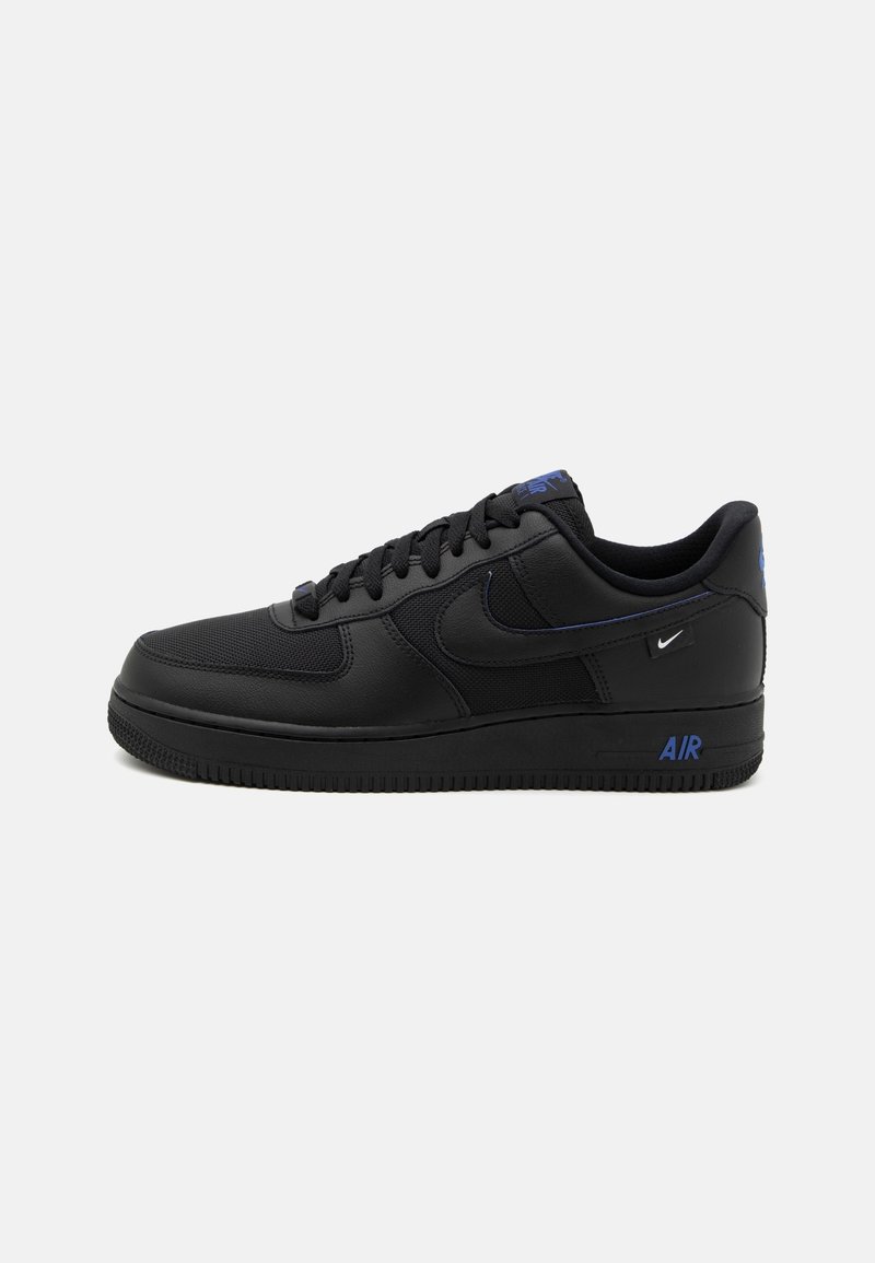 Baskets basses noires avec lacets noirs, texte bleu "AIR" sur la semelle et petits logos Nike blancs et bleus sur le côté et le talon.