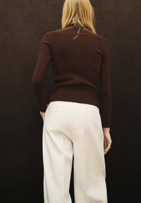 Jersey de cuello alto de canalé marrón combinado con pantalones blancos de cintura alta. El conjunto presenta mangas ajustadas y bolsillos laterales en los pantalones.
