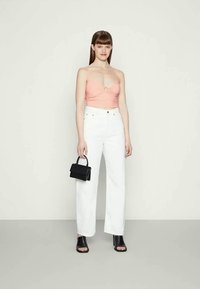 Top rosa com franzidos e detalhe em anel, jeans brancos de perna reta, sandálias de bloco pretas e uma pequena mala preta. Texturas suaves.