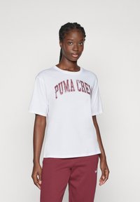 Camiseta de algodón blanca de manga corta, que presenta un gráfico burdeos "PUMA CREW" en el pecho, combinada con pantalones de chándal color burdeos.