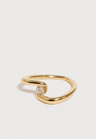 Guldring med åben bånd og en enkelt rund klar diamant fastgjort mellem enderne, sat mod en ensartet hvid baggrund.