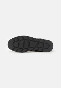 Suela de zapatilla de goma negra con un patrón texturizado, que presenta ranuras para tracción y un logo visible. Bordes lisos y secciones reforzadas.