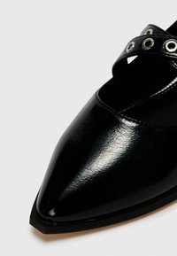 Zwarte puntige schoen van glanzend synthetisch materiaal, met een kruislings bandje en zilveren ogen. Gladde textuur en minimalistisch ontwerp.