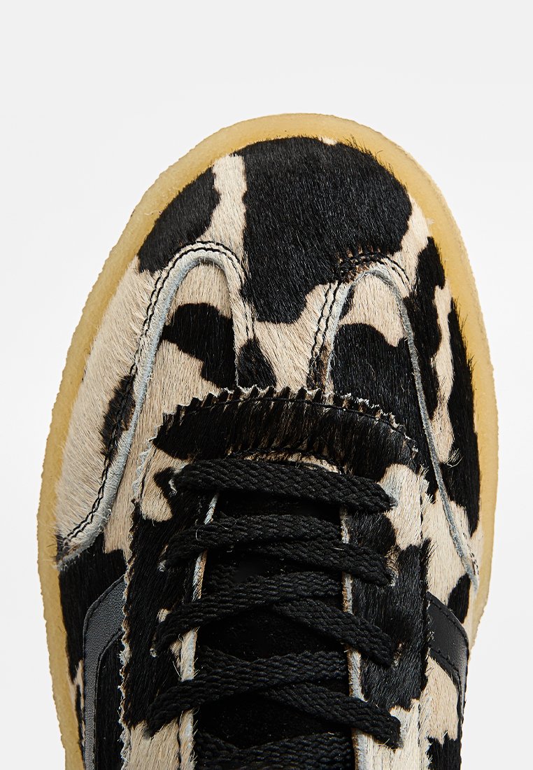 Schwarz-weißes Kuhflecken-Sneaker mit einem strukturierten Futter, schwarzen Schnürsenkeln und einer hellen Gummisohle. Verfügt über ein rundes Zehendesign.