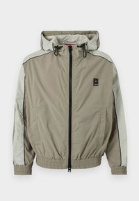 Μπεζ και ανοιχτό γκρι ζακέτα με κουκούλα και φερμουάρ, με ελαστικά μανίκια και τελείωμα, μαύρο λογότυπο στο στήθος και μπροστινές τσέπες.