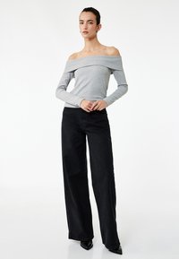 Szara bluzka off-the-shoulder z długim rękawem w połączeniu z wysokimi, czarnymi spodniami o szerokich nogawkach. Gładki materiał o minimalistycznym designie.