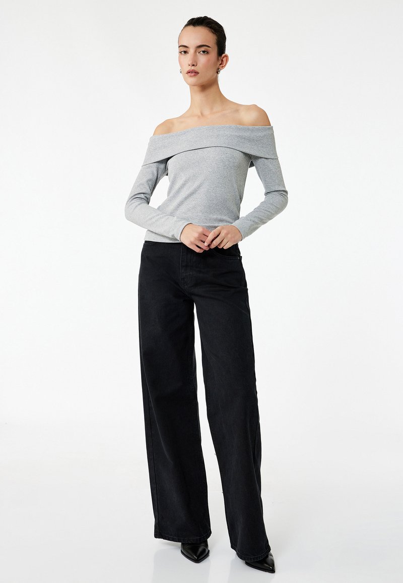 Szara bluzka off-the-shoulder z długim rękawem w połączeniu z wysokimi, czarnymi spodniami o szerokich nogawkach. Gładki materiał o minimalistycznym designie.