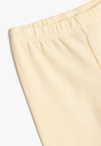 Tela de color crema, con ribetes y una cintura elástica, que muestra líneas verticales para dar textura. El material parece suave y elástico.