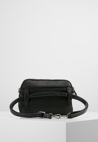 Musta synteettisestä nahasta valmistettu olkalaukku, jossa on sileä pinta, vetoketjukiinnitys, säädettävä hihna ja etutasku vaakasuoralla läpällä.