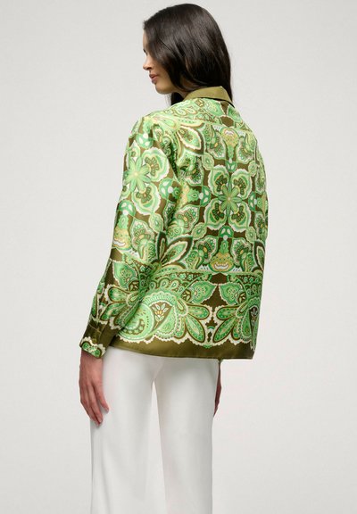 Chemise en satin dans des tons verts avec des motifs floraux et cachemires, dotée d'un col et de manches longues. Associée à un pantalon large blanc.