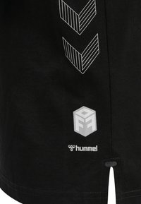 Svart t-shirt med vita geometriska mönster, med en logotyp med kubdesign och märkesnamnet "Hummel" vid den nedre fållen.