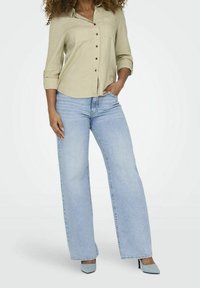 Lys beige skjorte med knapper og to forlommer, parret med lyseblå brede jeans og matchende blå højhælede sko.