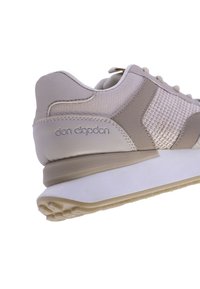 Zapatilla beige con cuero texturizado y paneles de malla. Presenta una punta redondeada, suela de goma y una marca en relieve en el costado.