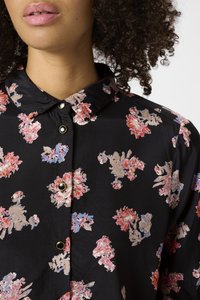 La chemise à motifs floraux noirs est dotée d'un col, de boutons dorés et de motifs de fleurs roses et bleues sur un tissu texturé.