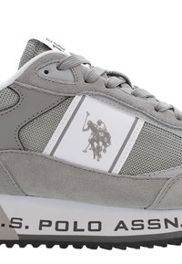 Šedá sportovní bota vyrobená z materiálů síťoviny a semiše, s bílou částí, která zobrazuje logo pólisty a černým textem na podrážce.