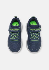 Mrežne tenisice u mornarskoj plavoj boji s zelenim akcentima, teksturiranim materijalom i čičak trakom. Imaju bijele gumene potplate i dekorativne šavove.