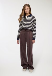Polo a maniche lunghe a righe con colletto blu navy, abbinata a pantaloni marroni larghi con vita elasticizzata e coulisse.