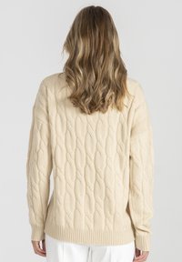 Beżowy sweter warkoczowy z teksturowanym wzorem, z ribbowanymi mankietami i hemem, z długimi rękawami i luźnym krojem.