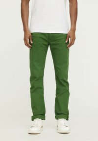 Pantalons en coton verts avec une coupe slim, dotés de poches et d'un ourlet roulé, associés à des baskets blanches et un t-shirt blanc uni.