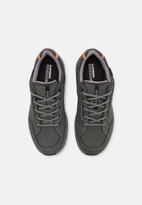 Sneakers grigi con tomaia liscia, punta rotonda, lacci a contrasto e collare imbottito. Presentano un accento marrone vicino al tallone.