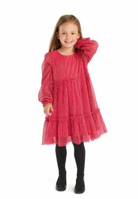 Robe rouge à manches longues avec une jupe à volants en couches et un tissu texturé. Assortie avec des collants noirs et des chaussures. Encolure ronde simple.