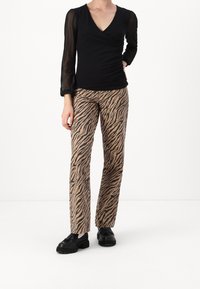 Top nero a maniche lunghe con scollatura a V e maniche trasparenti, abbinato a pantaloni a gamba larga in stampa animale, beige e marrone, e scarpe nere.