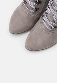 Botines de ante gris de corte por el tobillo con puntera afilada, que presentan cordones de cuadros en gris y blanco, ojales metálicos y una superficie texturizada.
