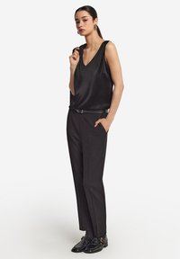 Svart satin ärmlös topp med V-hals, parat med skräddarsydda svarta byxor och glansiga svarta skor med guldaccenter.