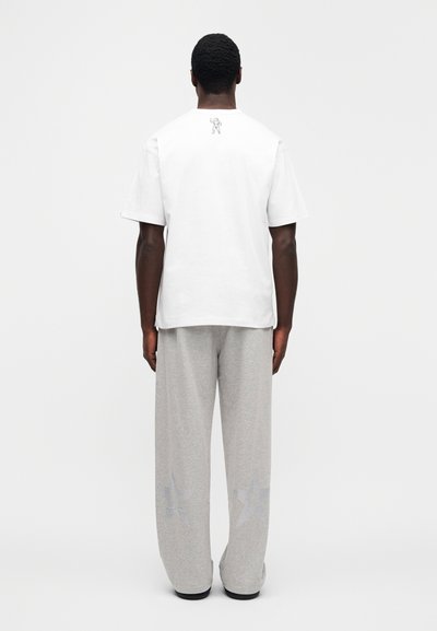 Λευκό βαμβακερό μπλουζάκι με γραφικό στην πλάτη, συνδυασμένο με ανοιχτό γκρι, άνετο παντελόνι φόρμας με σχέδια αστεριών κοντά στο τελείωμα.