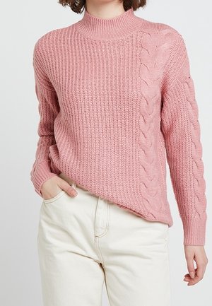 Rosa gestrickter Pullover mit hohem Ausschnitt, der auf einer Seite ein strukturiertes Rippdesign und auf der anderen Seite ein Zopfmuster aufweist.