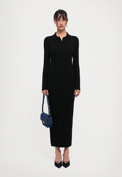 Robe noire à manches longues côtelées avec un col et une fermeture à boutons. Associée à un sac en denim bleu et des escarpins noirs à bout pointu.