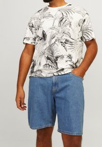 Bílé tričko s krátkým rukávem s černými tropickými listy, doplněné o světle modré džínové šortky po kolena. Ležérní střih a design.