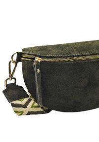 Sac en daim vert à texture lisse, avec une fermeture éclair dorée et une sangle en tissu à motif géométrique vert et beige. Accents métalliques élégants.