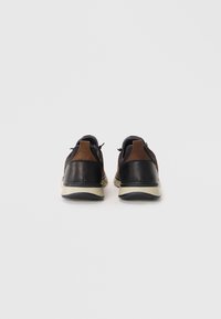 Chaussures en cuir noir et marron avec une finition texturée, bout rond, capot de talon contrastant et semelle en caoutchouc de couleur claire. Deux languettes à l'arrière.