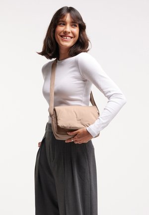 Beige padded shoulder bag with a fold-over flap and embossed logo. Soft texture, adjustable strap, and rectangular shape.