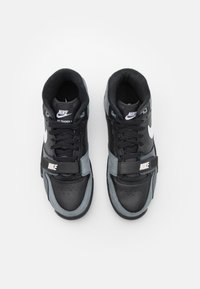 Adidași Nike Air Trainer 1 cu un superior din piele neagră, accente din nubuc gri, detalii de cusătură, vârf perforat și logo alb pe laterale.