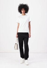 Witte t-shirt met korte mouwen en subtiele branding, gecombineerd met zwarte tapers. De outfit wordt aangevuld met witte sneakers en een lichte handtas.