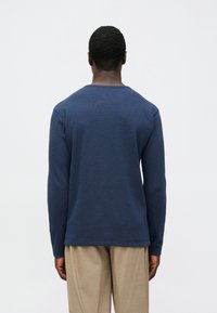 Camisola de manga comprida azul marinha texturizada, com decote redondo, punhos ajustados e barra reta, combinada com calças bege claro.