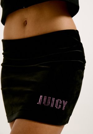 Mini-jupe en velours noir avec fronces, ornée d'un logo "JUICY" en strass roses en bas à droite. Texture lisse et design ajusté.