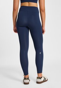 Leggings blu navy con vita alta, realizzati in tessuto liscio, con un piccolo logo a chevron bianco sulla parte bassa della gamba.