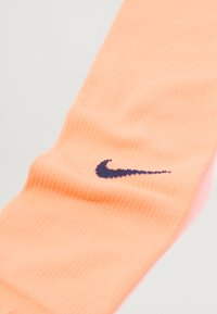 Nike zokni világos őszibarack színben, bordázott textúrával és sötét tengerészkék logóval, amely kiemeli a testhez simuló, áramvonalas dizájnt.