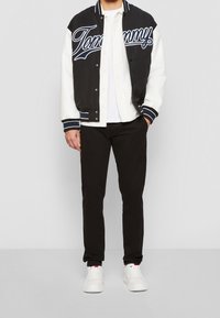 Černobílá varsity bunda s nápisem "Tommy", bílá košile, černé kalhoty a bílé tenisky. Klasický sportovní design a pohodlný střih.